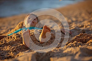 Child, tickling sibling on the beach on the feet with feather, kid cover in sand, smiling, laughing