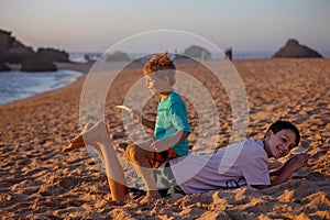 Child, tickling sibling on the beach on the feet with feather, kid cover in sand, smiling, laughing