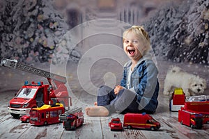 Child, toddler blond boy, playing with fire trucks on the floor