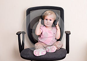 Child toddler in office chair and in headphones. Baby girl listening to music.