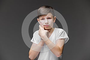 Child toothache. holding his cheek, dental pain. Closeup portrait boy with sensitive tooth. isolated grey wall background.