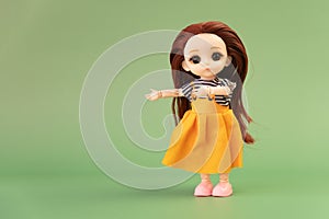 child toy doll with dark hair in an orange dress standing on a green background. Plastic children's toy. a plastic doll indicates