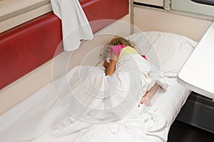 A child in train sleeping wrapped in a sheet in the lower place in the second-class compartment wagon
