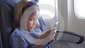 Child Traveling by Plane, Kid Playing Tablet in Airplane, Little Girl Using Smartphones by Window, Children Traveling in Vacation