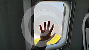 child travels by plane, little boy holds his hand on plane window during the flight closeup
