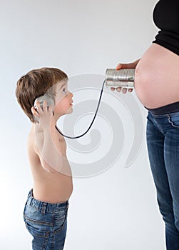 Child trying to listen inside the belly of a pregnant woman with a tin can phone