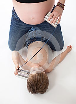 Child trying to listen inside the belly of a pregnant woman with a tin can phone