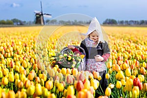 Child in tulip flower field. Windmill in Holland.