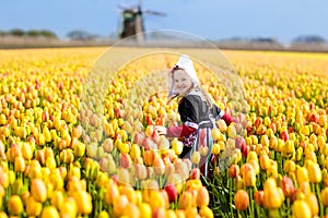 Child in tulip flower field. Windmill in Holland