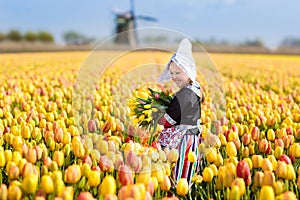 Child in tulip flower field. Windmill in Holland