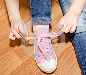 Child tying her shoes sitting on the floor