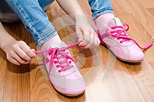 Child tying her shoes sitting on the floor at home