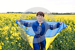 Child with Ukrainian flag in rapeseed field. A girl in an embroidered shirt runs across the field with the Ukrainian flag in her