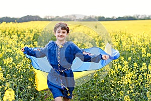 Child with Ukrainian flag in rapeseed field. A girl in an embroidered shirt runs across the field with the Ukrainian flag in her