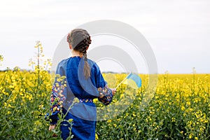 Child with Ukrainian flag in rapeseed field. A girl in an embroidered shirt runs across the field with the Ukrainian flag in her