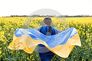 Child with Ukrainian flag in rapeseed field. A girl in an embroidered shirt runs across the field with the Ukrainian flag in her