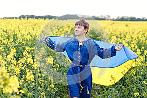 Child with Ukrainian flag in rapeseed field. A girl in an embroidered shirt runs across the field with the Ukrainian flag in her