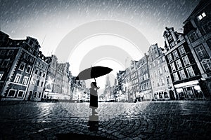 Child with umbrella standing alone on cobblestone old town in rain