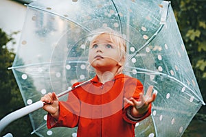 Child with umbrella wonders rainy weather walking outdoor toddler girl wearing red raincoat autumn season