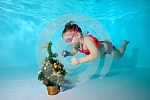 Child underwater in the pool decorates the Christmas tree with Christmas toys. Portrait. Shooting under water. Horizontal orientat