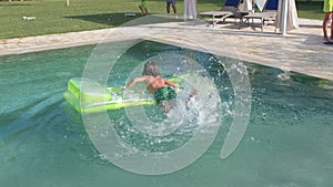 Child uses inflatable mattress while swimming in pool during summer vacations.