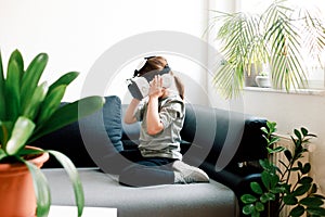 Child using black-white 3D Virtual Reality glasses sitting on sofa