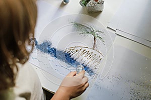 Child using blue glitter sparkles from the jar for create a picture