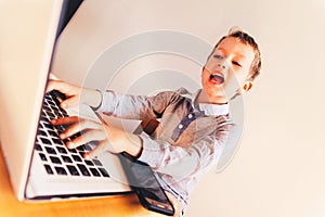 Child using a laptop and celebrating with gestures his success in business by earning a lot of money