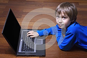Child using laptop PC lying on wooden floor. Top view. Education, learning, technology concept