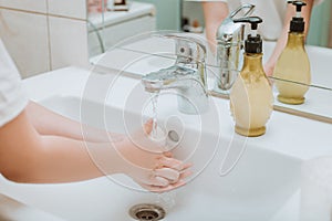 Child using soap and washing hands under the water tap.