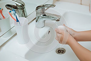 Child using soap and washing hands under the water tap.