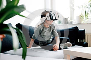 Child in virtual augmented reality helmet sitting on sofa