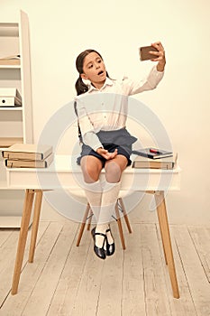 Child vlogger stream online. Child school uniform smart kid video conferencing while sit table. Girl holds smartphone