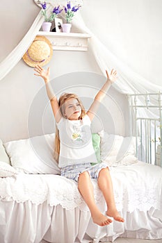 Child wakes up in morning in bed and stretches. Lazy girl happy waking up in bed rising hands to window in morning with feeling re