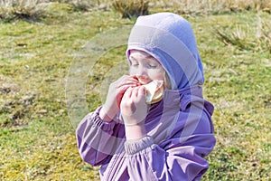 A child on a walk eats a sandwich on a spring sunny day.