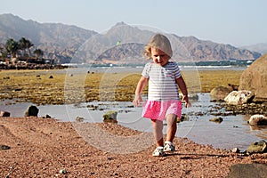 Child walking on coast against backgroun mountains