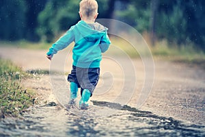 Child walking in wellies in puddle on rainy weather photo