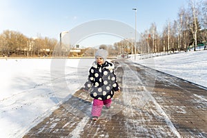 Child walks along the wide embankment of a frozen pond in winter