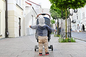 A child walks around the city with a stroller. Back view