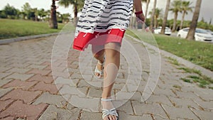 Child walks through a palm alley at sunset, rejoices and sings