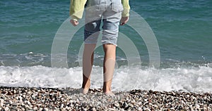 Child walks on seashore and wets feet