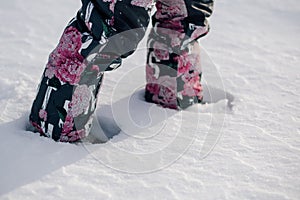 Child walks through snowdrift. Close-up view of children legs in warm pants with image of flowers walking along snowy