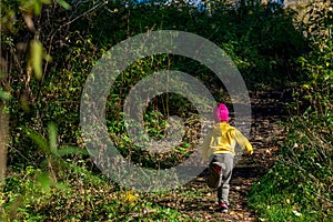 A child, in warm clothes and a red cap runs away along the path in the dark autumn forest