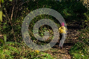 A child, in warm clothes and a red cap runs away along the path in the dark autumn forest