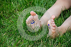The child was lying on the green grass. Smile with paints on the legs and arms. Child having fun outdoors in the spring