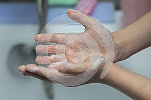 A child washes his hands in front of a faucet with water in the bathroom. Close-up photo