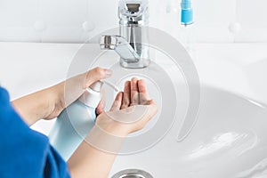 A child washes his hands near a white sink. The concept of hand hygiene and disinfection