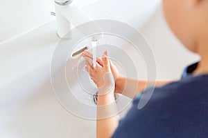 The child washes his hands in the sink under running water.