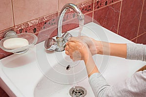 Child washes his hands under running water in the sink