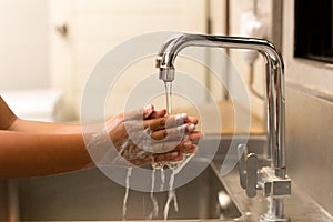 Child washing hands with liquid soap under the tap water